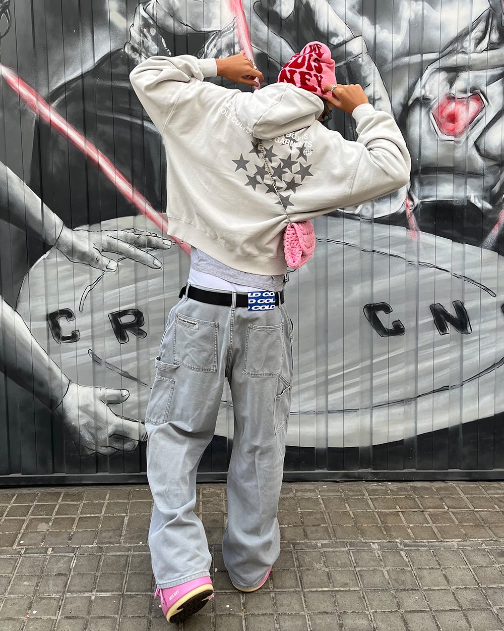 Source photograph: street-style shot of the hoodie against a painted roller shutter, arms raised